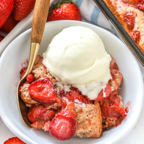 Strawberry Rhubarb Cobbler in a white bowl with vanilla ice cream and a spoon