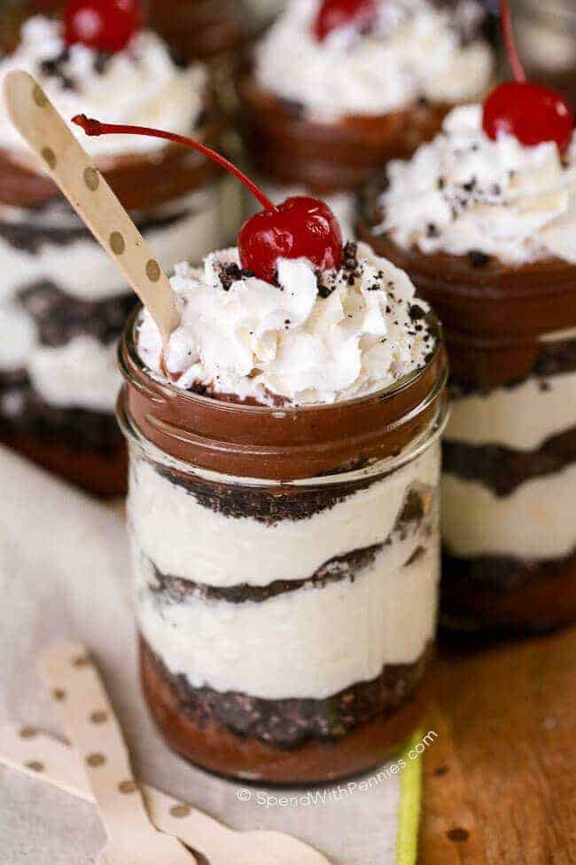 Oreo Chocolate Cheesecake Parfait in a blass mug with cherry on top and a wooden spoon in it