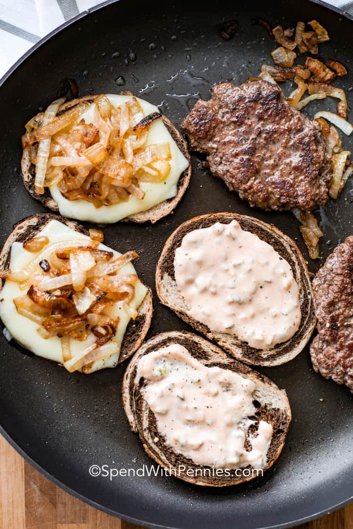 Treat your family to this mouthwatering patty melt recipe, a retro diner classic that you can make at home. This cross between a burger and grilled cheese sandwich features layers of ground beef, sautéed onions, Swiss cheese and tangy Thousand Island dressing, sandwiched between two slices of buttered sourdough bread. For best results, use thick slices of dense bread. The sandwich is grilled until melted, crunchy and golden brown for a tasty and irresistible lunch or dinner. #spendwithpennies Homemade patty melts in a pan