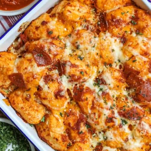 Pizza bubble bread in a casserole dish with pizza sauce and parsley on the side