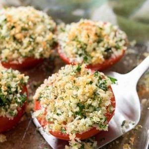 Oven Roasted Tomatoes in a clear baking dish, lifting one out with a spatula