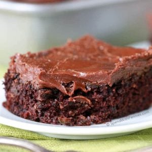 Zucchini Brownie on a white plate with fork in foreground and pan of them in the background