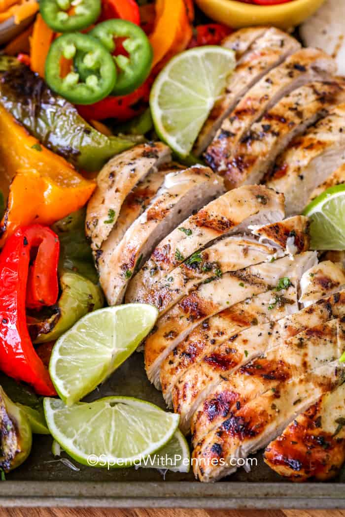 Ingredients for grilled chicken fajitas on a baking sheet with lime wedges