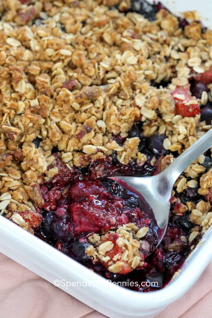 Homemade mixed berry crisp is a tasty dessert that perfectly combines comfort and simplicity. This yummy treat combines fresh or frozen strawberries, blueberries, and raspberries, creating a burst of flavorful goodness in every mouthful. You can enjoy it warm with a scoop of vanilla ice cream or as a refreshing summer treat when served cold. No matter how you choose to indulge, homemade mixed berry crisp is guaranteed to please anyone with a sweet tooth. #mixedberrycrisp #berrycrisp #dessert #homemade #spendwithpennies Mixed Berry Crisp in a baking dish with serving spoon