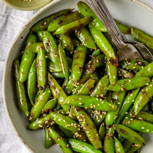 snap peas garnished with sesame seeds in a bowl with a fork and spoon
