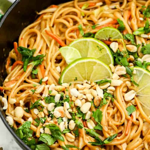 Peanut Thai noodles in a pot with peanut cilantro and lime wedges on top