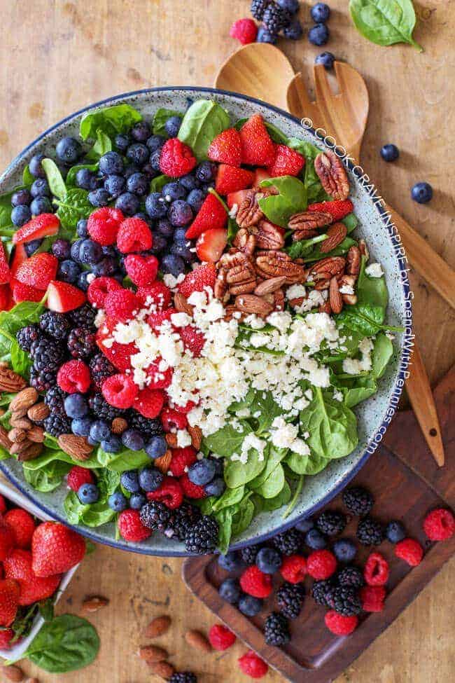 Overhead shot of Fruit & Nut Spinach Salad with wooden spoons on a cutting board