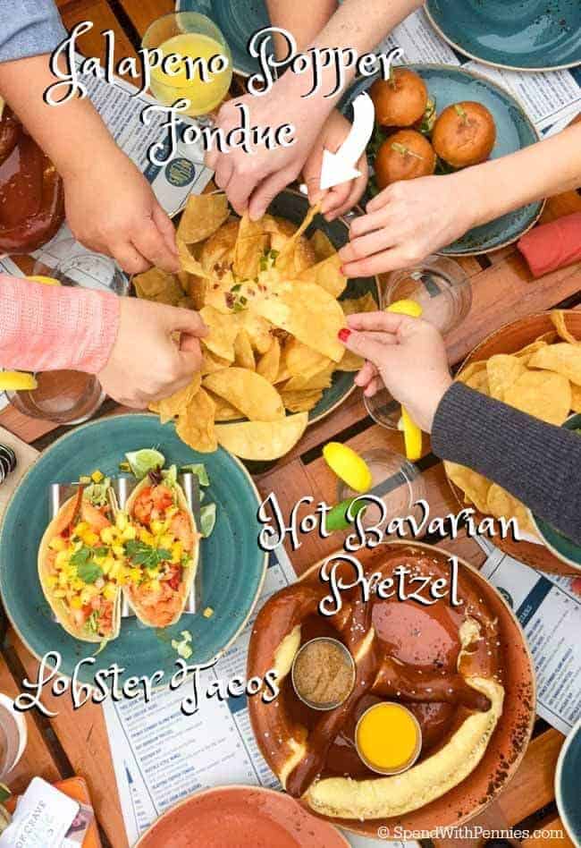 Overhead shot of people reaching for jalapeno popper fondue, along with lobster tacos and hot bavarian pretzel