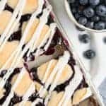 Overhead shot of Removing a Blueberry Pie Bar from the baking sheet and a bowl of blueberries