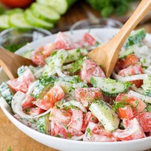 Creamy Cucumber Tomato Salad in a white bowl with wooden spoons
