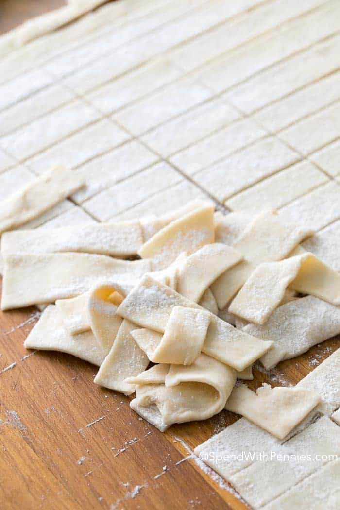 Make this old fashioned chicken and dumplings recipe for a classically comforting dish. What's not to love about the easy recipe? It all begins with simple ingredients and simple steps. A whole chicken is simmered with some vegetables and then topped with homemade strips of biscuit dough. So delicious! #spendwithpennies Lots of dough strips on a cutting board