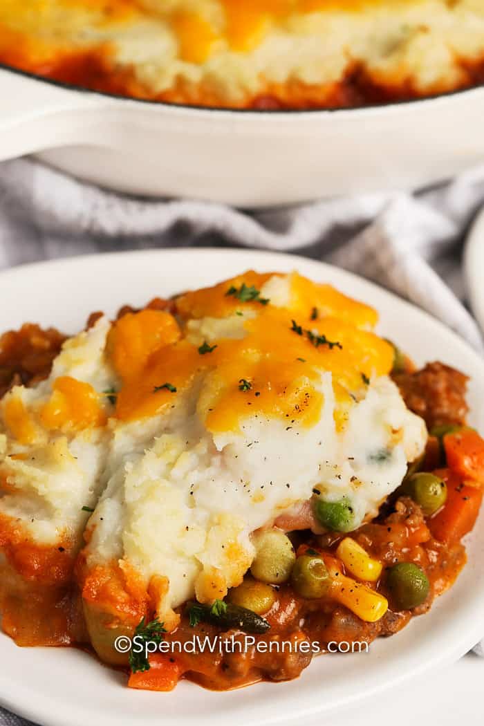 Shepherd's Pie is the perfect dish to serve for St. Patricks Day! We love this super tasty and comforting dish, loaded with ground meat and veggies in a savory sauce, a mashed potato crust, and finally topped with cheese and baked! #shepherdspie #groundlamb #groundbeef #spendwithpennies Shepherd's Pie Recipe on a white plate with parsley