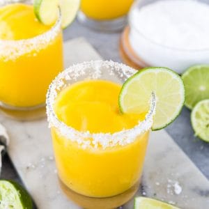 Frozen mango margaritas in round glasses with salt rims and lime wedge with salt and lime on the side