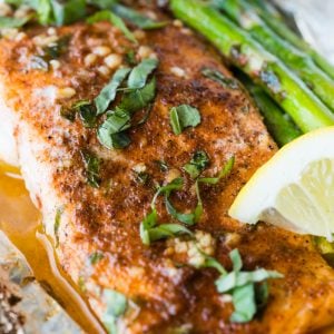 A fillet of salmon sitting on foil with a lemon wedge and asparagus