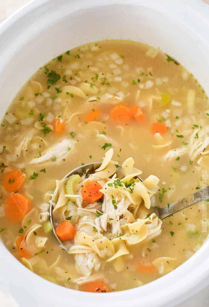 Ladle of crockpot chicken noodle soup in slow cooker