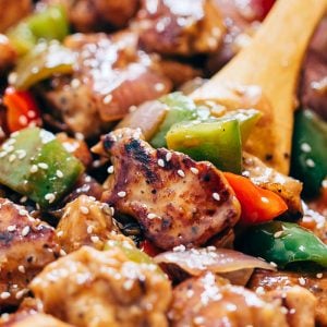 Close up of pepper chicken stir fry in a pan with a wooden spoon