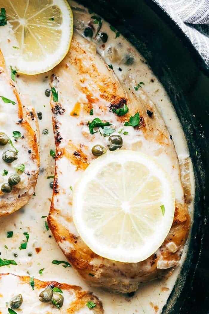 Closeup of creamy lemon chicken scallopini in a skillet with capers and lemon slices