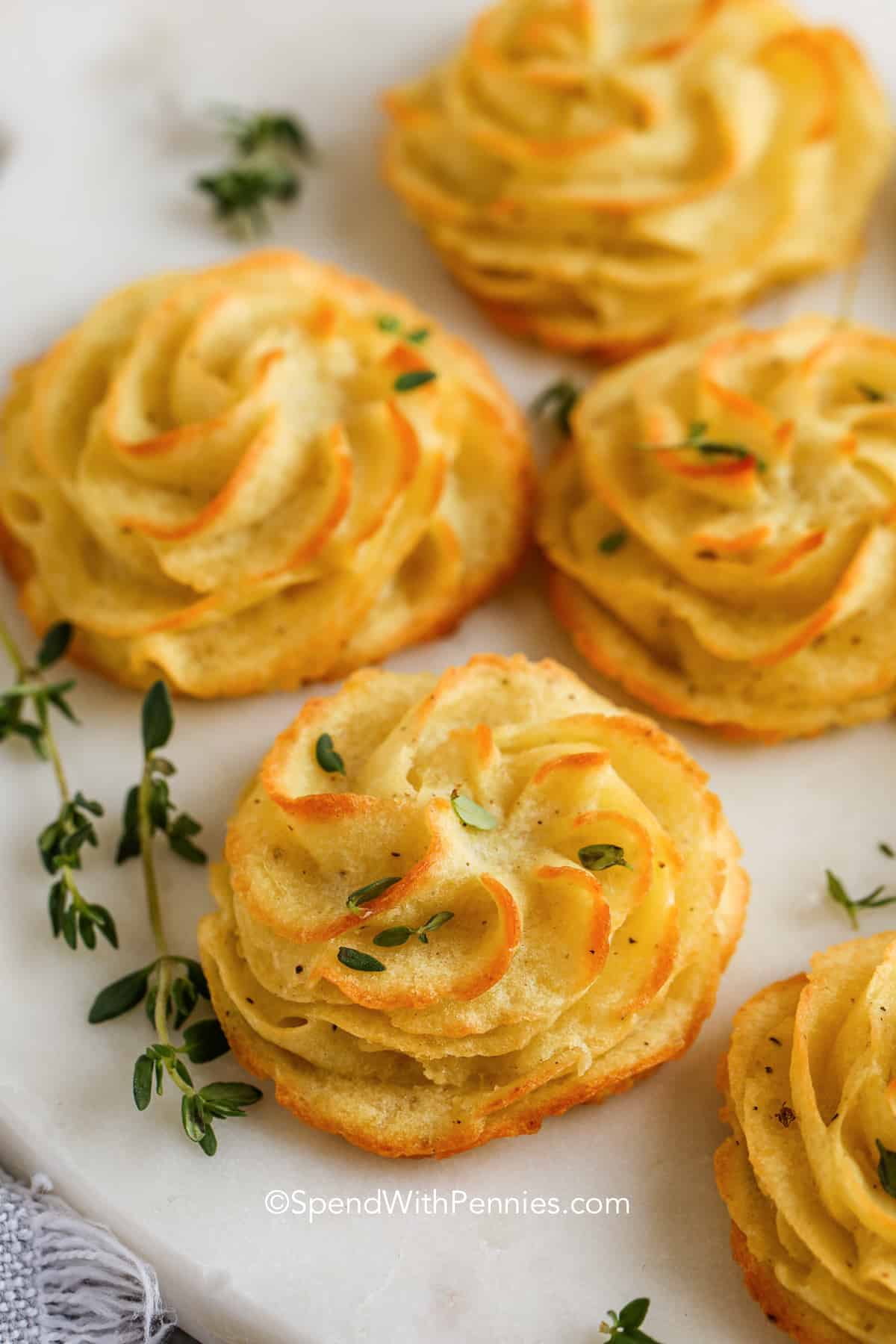 This recipe for duchess potatoes creates beautifully piped potato swirls with crisp edges and rich flavor. Russet potatoes keep the mixture light, while egg yolks add a velvety texture. Baking transforms the swirls into a golden, elegant side. These potatoes pair well with roasted meats and can be prepared ahead of time for convenience. #spendwithpennies close up of duchess potatoes with thyme