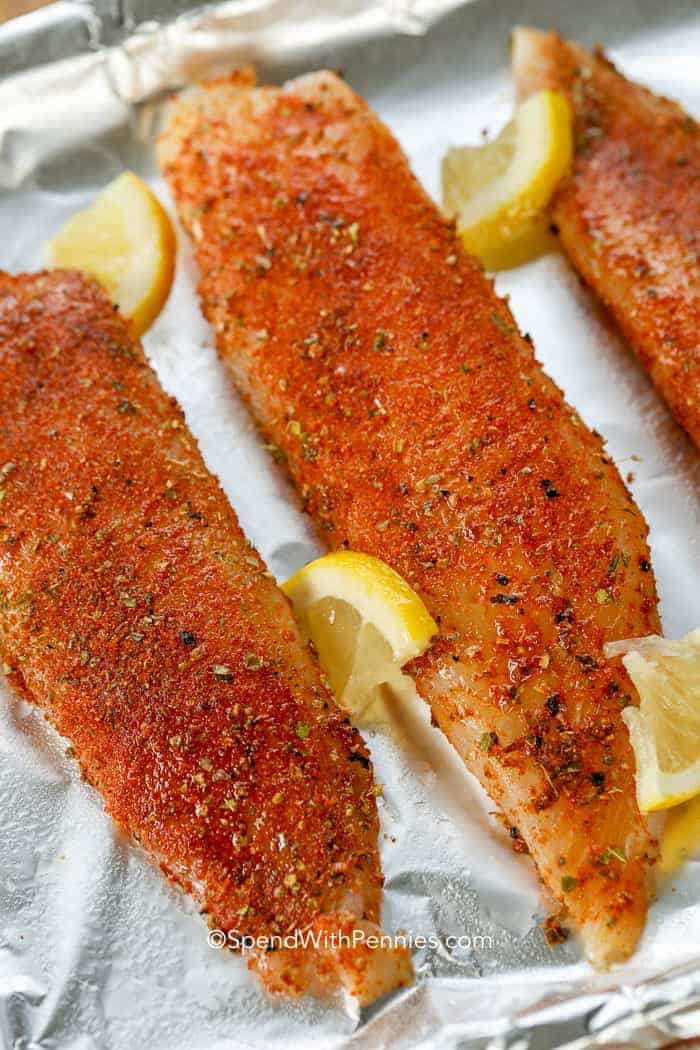 Pan fry a batch of blackened tilapia and take the stress out of cooking dinner on hectic evenings. Coat tilapia fillets with a flavorful mix of herbs, spices, and a hint of brown sugar. Sizzle the seasoned fillets in butter and oil, or pop them in the oven to broil briefly on each side. Finish it off with a squeeze of lemon, and serve alongside rice and cole slaw for a satisfying dinner! #blackenedtilapia #blackenedtilapiarecipes #spendwithpennies #blackenedtilapiabaked Uncooked tilapia with lemon slices on baking sheet ready to go into oven