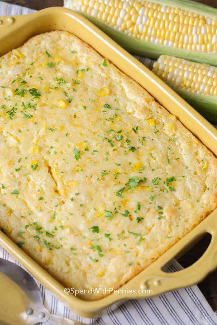 Yellow baking dish of Corn Casserole with ears of corn next to it