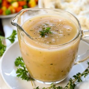 Turkey gravy in a clear glass pouring cup on a white plate