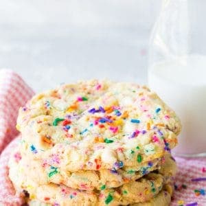 White Chocolate Funfetti Sugar Cookies, a stack of 3, with a glass of milk behind, sitting on a pink napkin