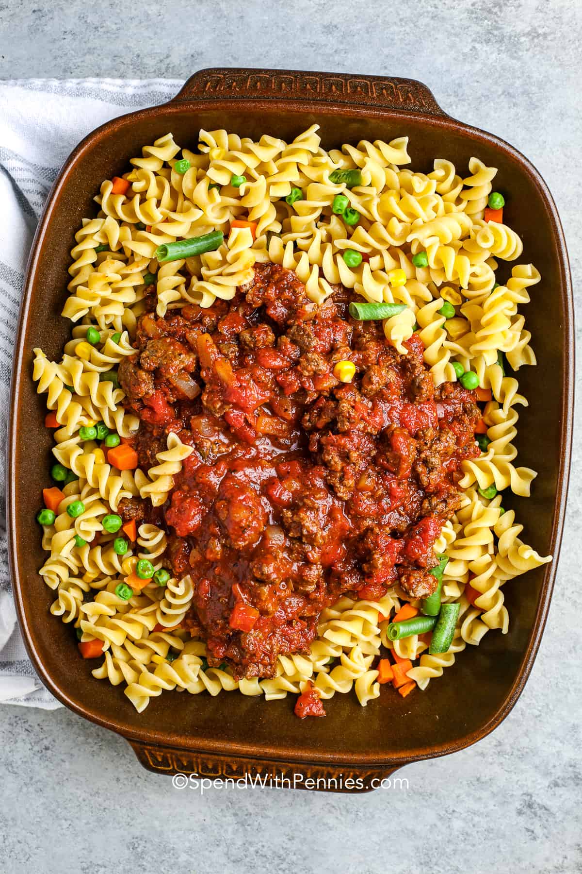 Hamburger casserole is a full-flavored recipe combining meat, veggies, and pasta in one pan. You can imagine variations using macaroni, rotini, or even rice in place of noodles. Add diced potato or mushroom pieces for texture. The tomato-based sauce is rich and savory, and the melted cheese finish gives it that perfect gooey bite. It’s reliable, hearty, and easy to love. #spendwithpennies sauce, noodles and vegetables in a casserole dish for hamburger casserole