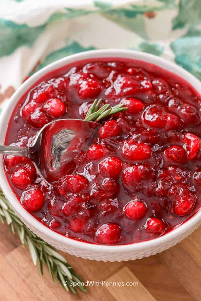 A bowl of fresh cranberry sauce topped with rosemary and a silver spoon.