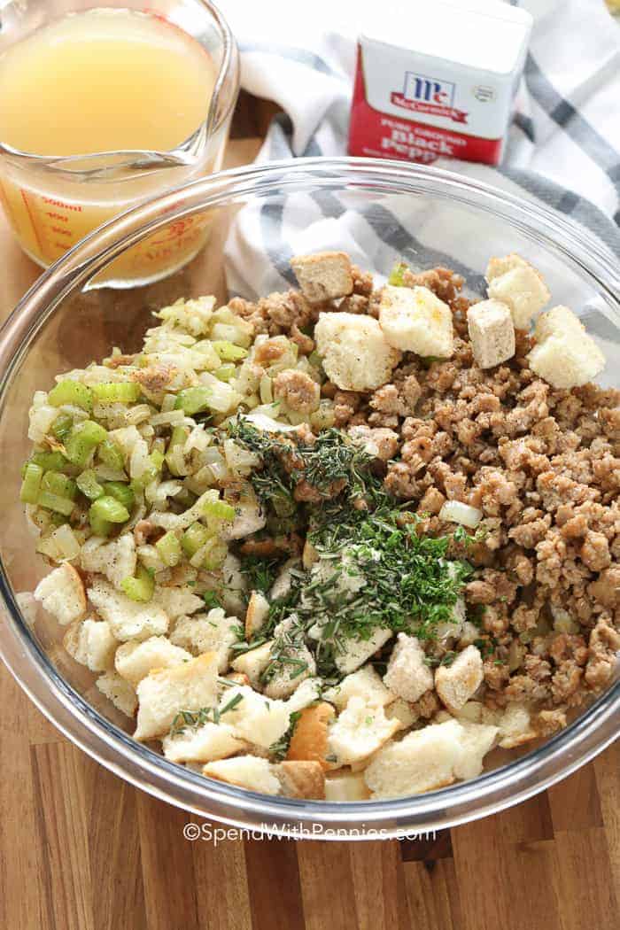 This best-ever sausage stuffing recipe combines ground pork sausage with savory sautéed onions and celery, enhanced by fresh sage for an aromatic touch. For a unique twist, add mushrooms or diced apples to complement the flavors. Ideal for turkey, this stuffing absorbs rich chicken broth and is seasoned with Italian herbs. With its comforting texture, it pairs perfectly with roasted meats and cranberry sauce, making it a delicious holiday staple that everyone will love! #spendwithpennies unmixed ingredients of stuffing in a dish