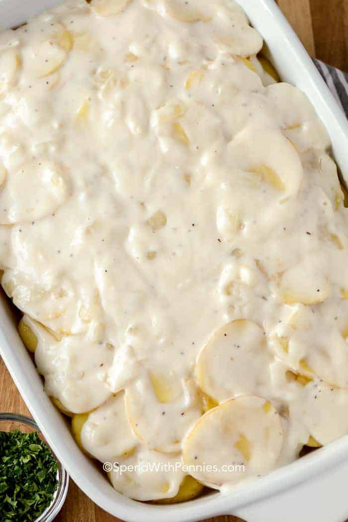 The foundation for these scalloped potatoes is a good roux. A roux is a sauce made by cooking flour with fat (in this case butter) and adding liquid to thicken, making a creamy sauce! #spendwithpennies #easyrecipe #scallopedpotatoes #potatorecipe #creamypotatoes #sidedish #easysidedish #festiveside #thanksgiving #casserole #easycasserole #roux A pan of raw scalloped potatoes with parsley on the side