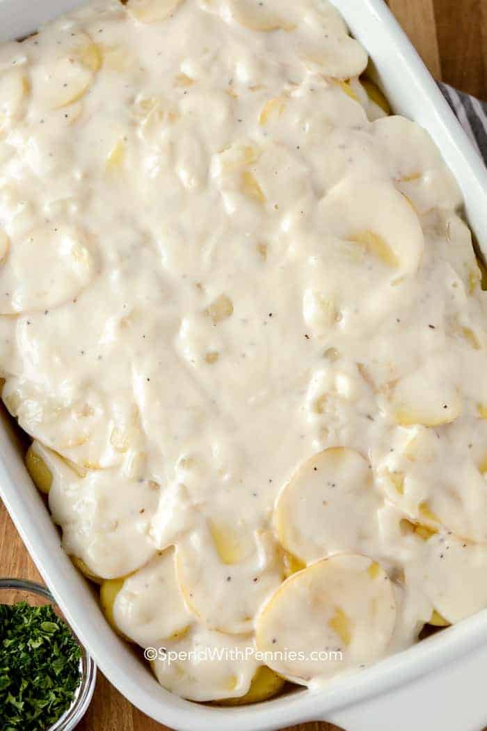 A pan of raw scalloped potatoes with parsley on the side