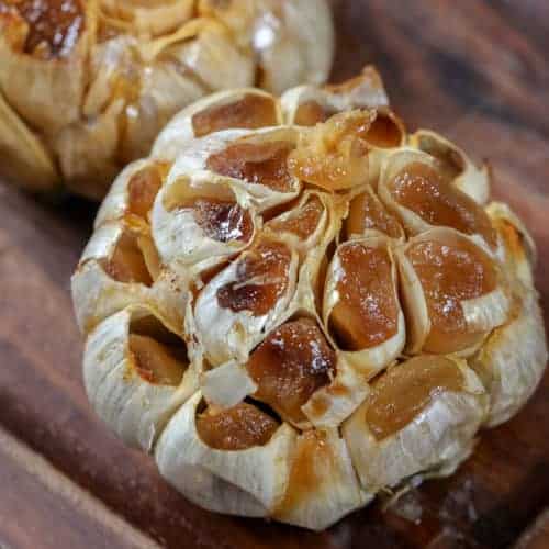 two heads of Roasted garlic on a wood board