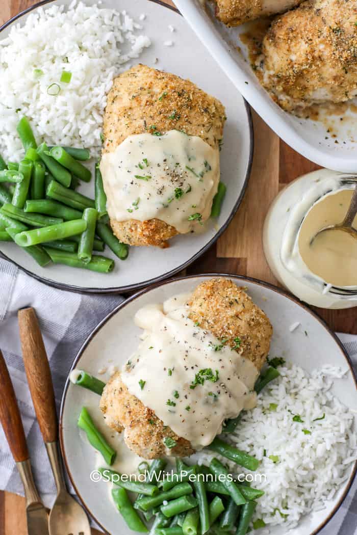 Chicken Cordon Bleu is an easy classic. Tender chicken breasts are stuffed with smoky ham and Swiss cheese, then baked until perfectly golden. Serve with simple dijon cream sauce for the best entree ever! #chickencordonbleu #entree #maindish #spendwithpennies Overhead shot of two plates of Chicken Cordon Bleu served with rice and green beans