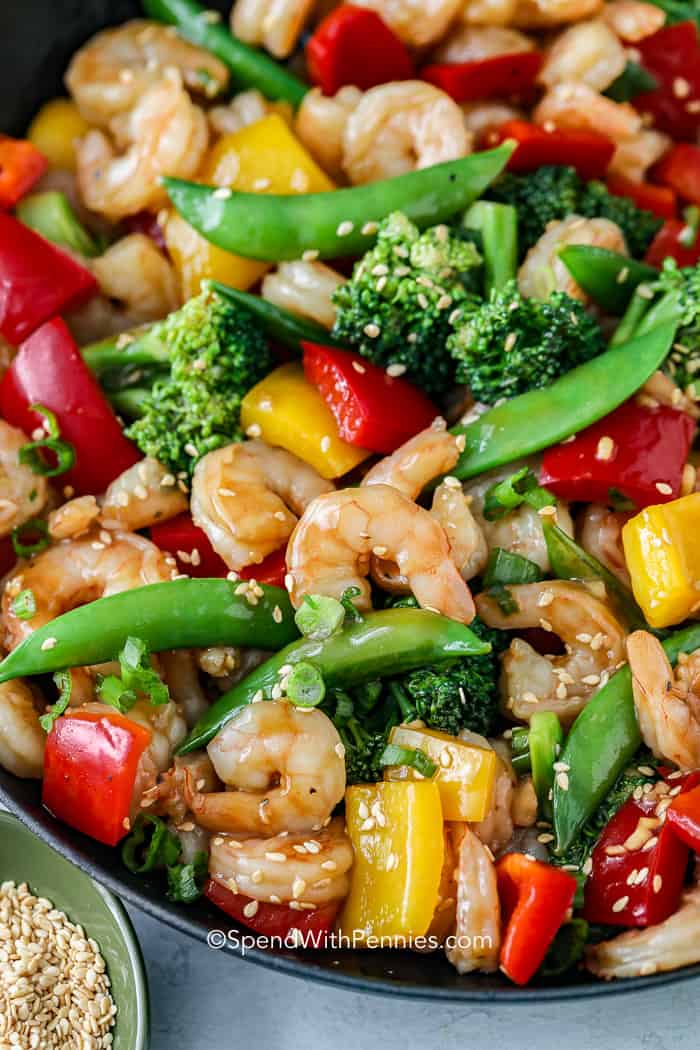 Shrimp stir fry in a pan with sesame seeds and green onions on top