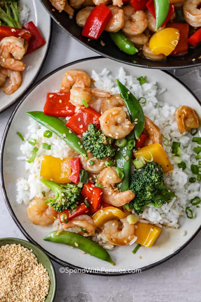 An overhead shot of shrimp stir fry on a bed of rice on a white plate.