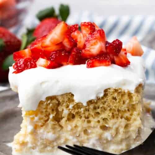 A slice of tres leches cake on a pewter plate, cake is topped with strawberries