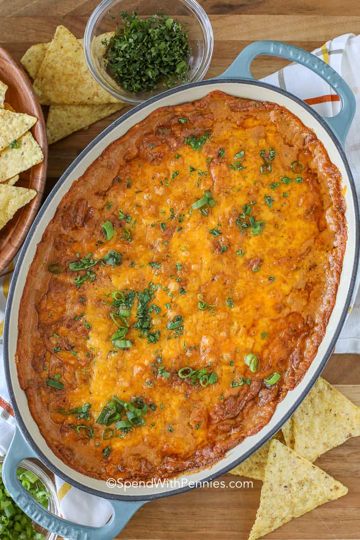 Creating a simple and tasty bean dip is a breeze with a base of cream cheese and refried beans. Just mix in some zesty taco seasoning with loads of cheese and kick it up a notch with jalapeños for a flavor-packed dip that's perfect for any fiesta! #beandip #refriedbeandip #appetizer #spendwithpennies Overhead shot of Bean Dip in an oval baking dish surrounded by tortilla chips