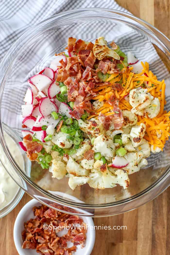 Make this loaded cauliflower salad as a keto side dish. Crispy cauliflower, spicy radishes, and celery are tossed with bacon and a creamy dressing for the best summer salad. No cauliflower? No problem. Simply replace it with broccoli. #loadedcauliflowersalad #cauliflowersalad #cauliflowersaladrecipe #spendwithpennies Cauliflower Salad ingredients in a clear glass bowl before being mixed together