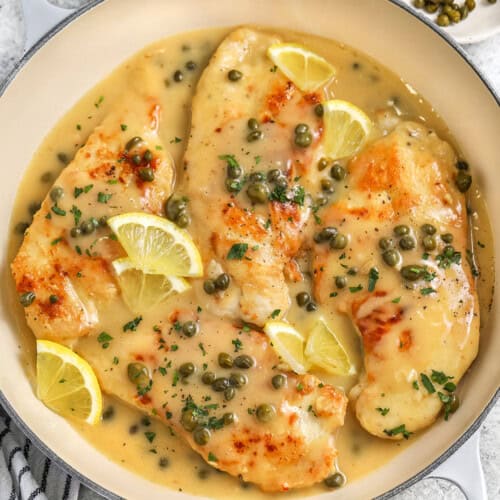 a skillet of chicken piccata with lemon slices and capers