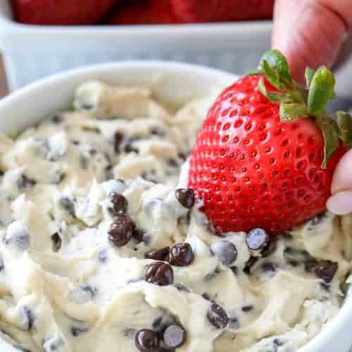 Cookie dough dip in a white bowl with a strawberry being dipped in
