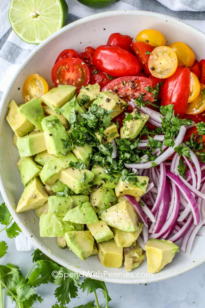 Bring this easy tomato avocado salad to the next backyard BBQ or potluck. Made with cherry tomatoes and drizzled with a simple olive oil dressing, this salad is one for the recipe box. This is so easy to make and is the perfect accompaniment to grilled chicken or salmon, shrimp, or steak. #tomatoavocadosalad #spendwithpennies #bestsummersaladrecipes #coldsalad Avocado salad in a white bowl with cilantro