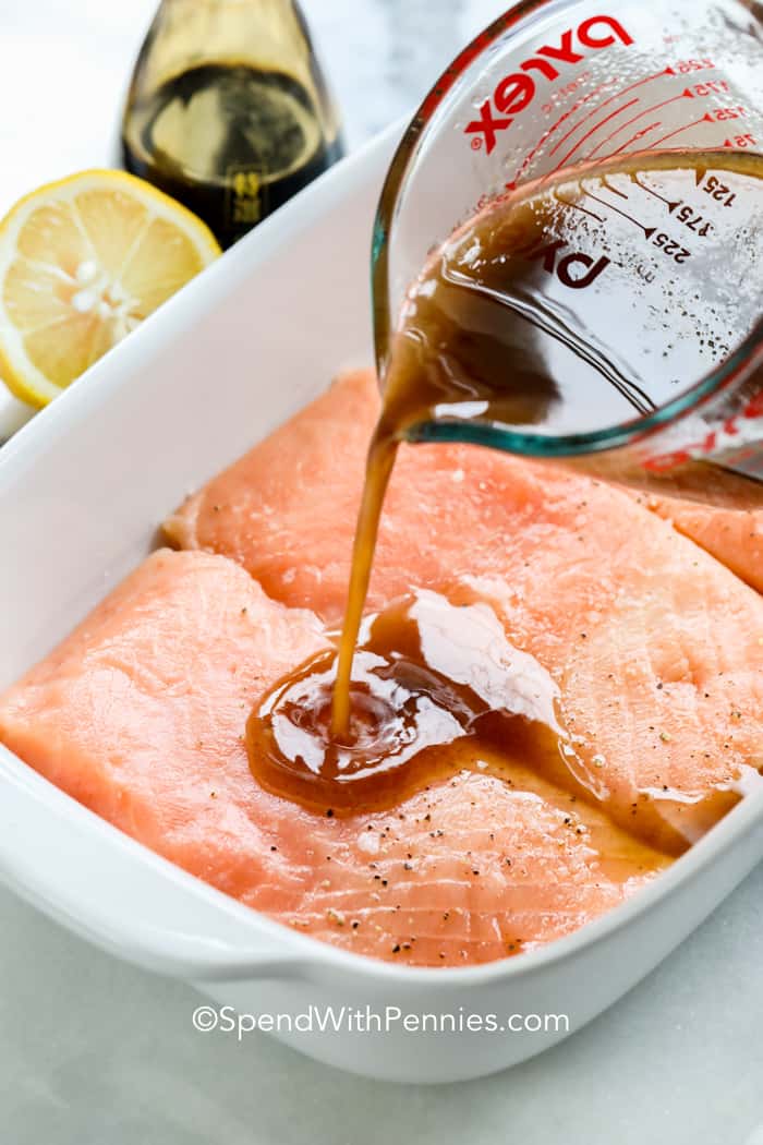Salmon fillets in a casserole dish with sauce being poured on