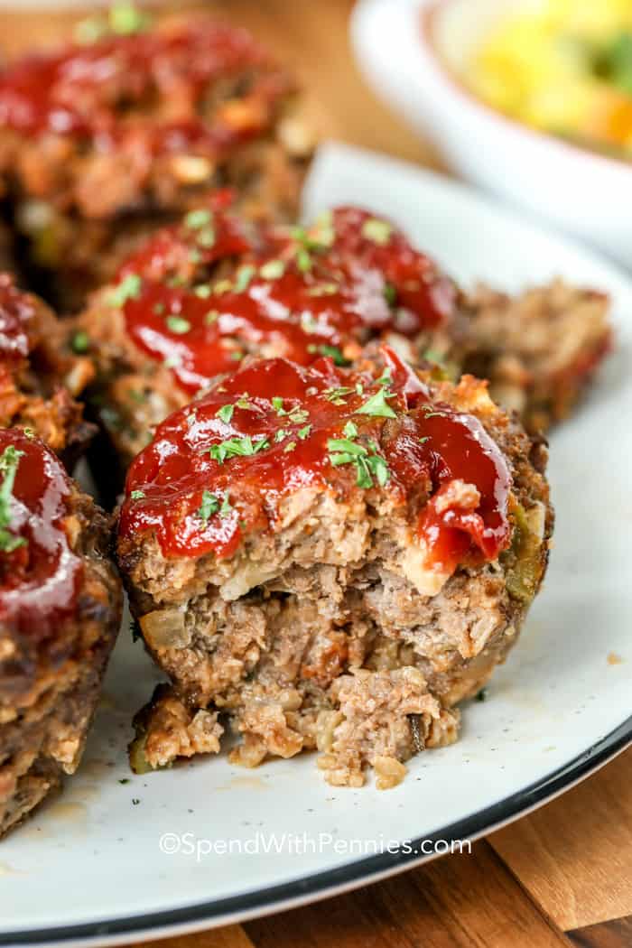 My family loves these mini meatloaf muffins. Made with either ground beef, turkey, or chicken and topped with a brown sugar glaze, they are easy to prepare and perfect for the freezer. Just reheat and serve as a snack, lunch, or dinner with mashed potatoes. #spendwithpennies #meatloafmuffins #meatloafrecipe #minimeatloaf Meatloaf Muffins on a plate with sauce