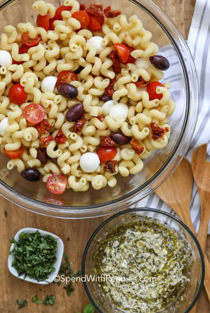 It won't take long at all to make this homemade pesto pasta salad. Simply toss some rotini noodles or other pasta with a tasty homemade dressing made from creamy pesto and add some cheese, sun-dried tomatoes, and olives. Other add-ins like chicken or avocado add so much classic flavor, and feel free to throw in other extras like spinach, too! #pestopastasalad #recipescold #pastasalad #spendwithpennies Pesto Pasta Salad ingredients in a bowl