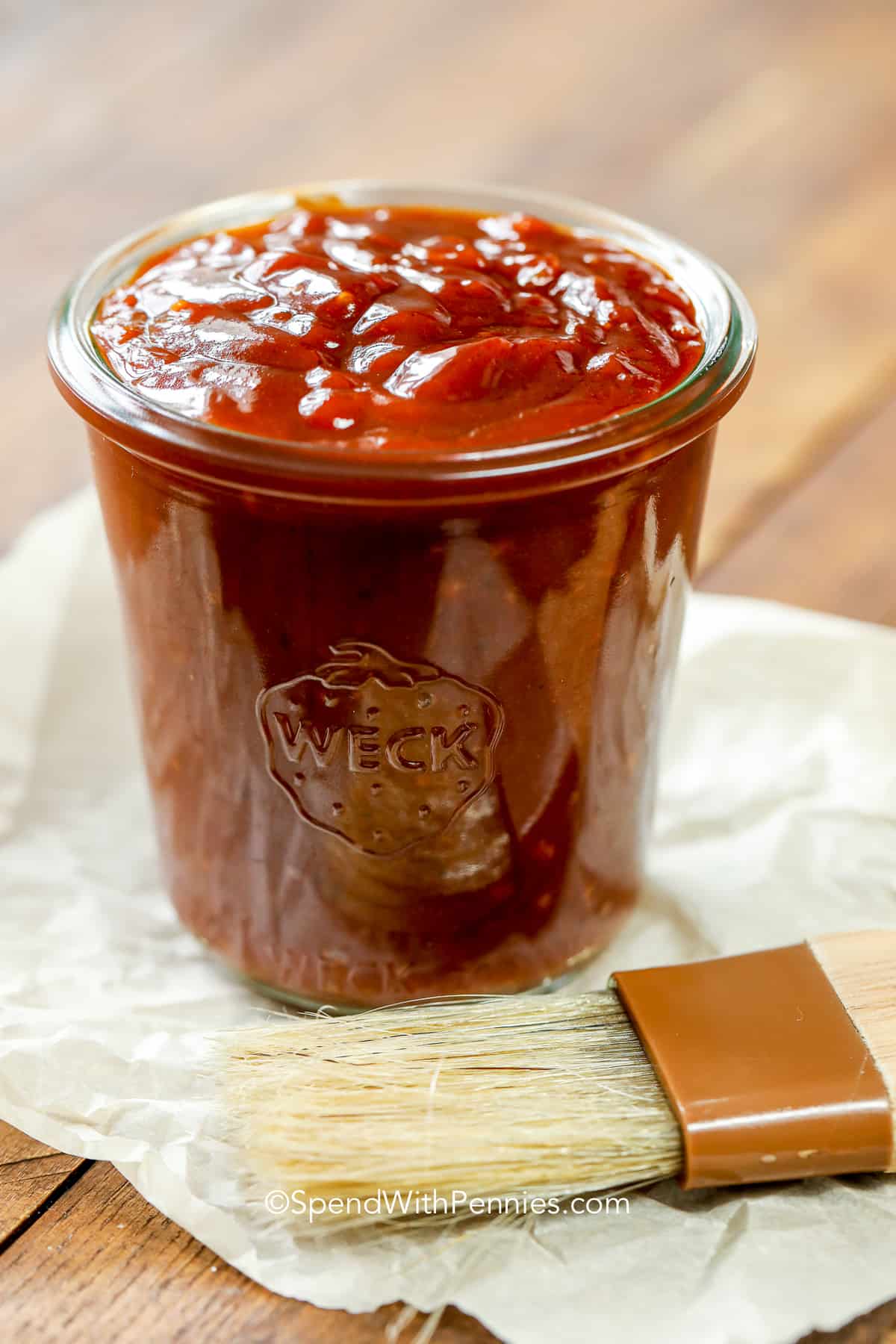 This homemade BBQ sauce recipe is so versatile and can be altered to choose any taste preference. Like your BBQ sauce sweet, tart, or spicy? Then look no further, this recipe is so easy to adjust. It is also so easy to make and is the best addition to any meal, whether it be those BBQ ribs, pork chops, or barbequed chicken breasts. #BBQsaucerecipe #BBQsauce #barbecuesauce #spendwithpennies a jar of homemade bbq sauce with a brush