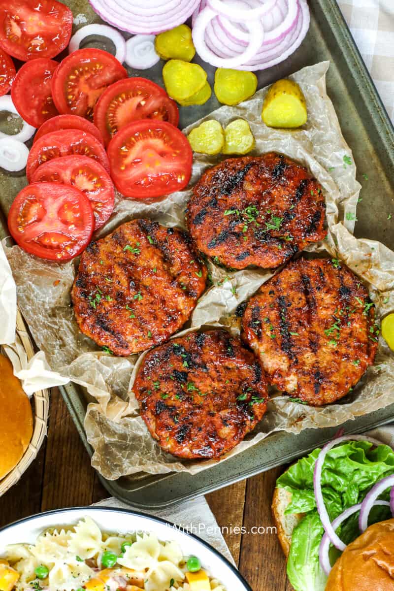 Make a double batch of these easy turkey burgers, and keep some frozen for quick weeknight meals that can be cooked up in a hurry on the grill or in the oven. It won't take long to make this recipe, just grab a package of ground turkey and add some tasty seasoning for the best quick burgers. #turkeyburgers #turkeyburgersrecipe #groundturkey #spendwithpennies cooked turkey patties on parchment paper with veggies