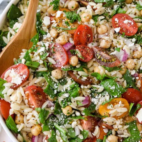 serving orzo pasta salad with a wooden spoon
