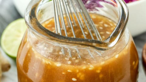 Sesame Ginger Dressing in a jar with a whisk and salad in the background