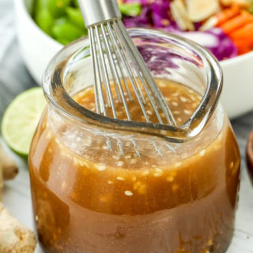Sesame Ginger Dressing in a jar with a whisk and salad in the background