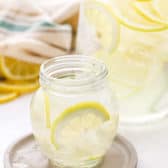 Small glass of Lemon Water with a big jar of it in the background